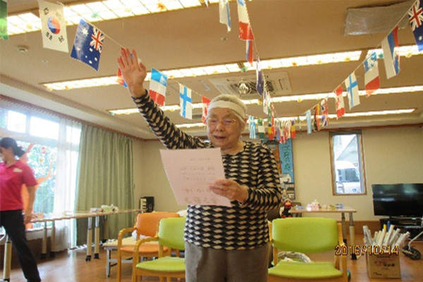 入居者が国旗装飾の下で手を上げて楽しくレクリエーションに参加している様子